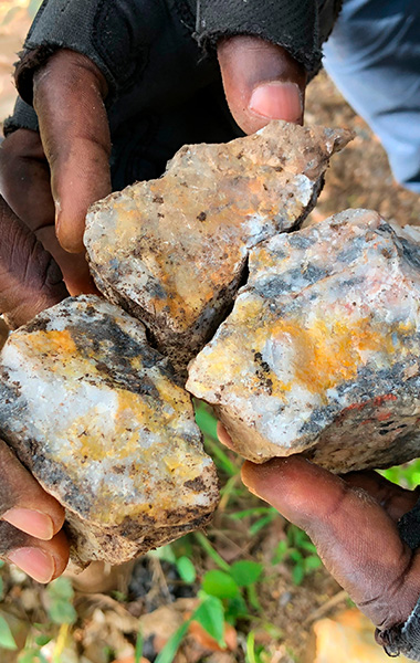 three artisan miners holding gold ore in rocks 